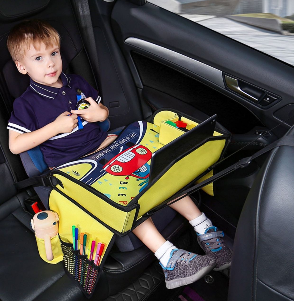 Child using a yellow kids car seat travel tray in the back seat