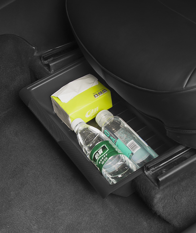 Black under-seat storage tray holding bottles and tissues beneath a Tesla Model Y seat